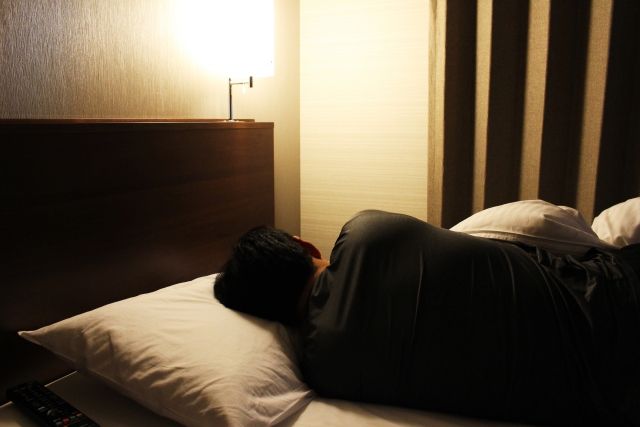 ビジネスホテルのベッドで横になる男性